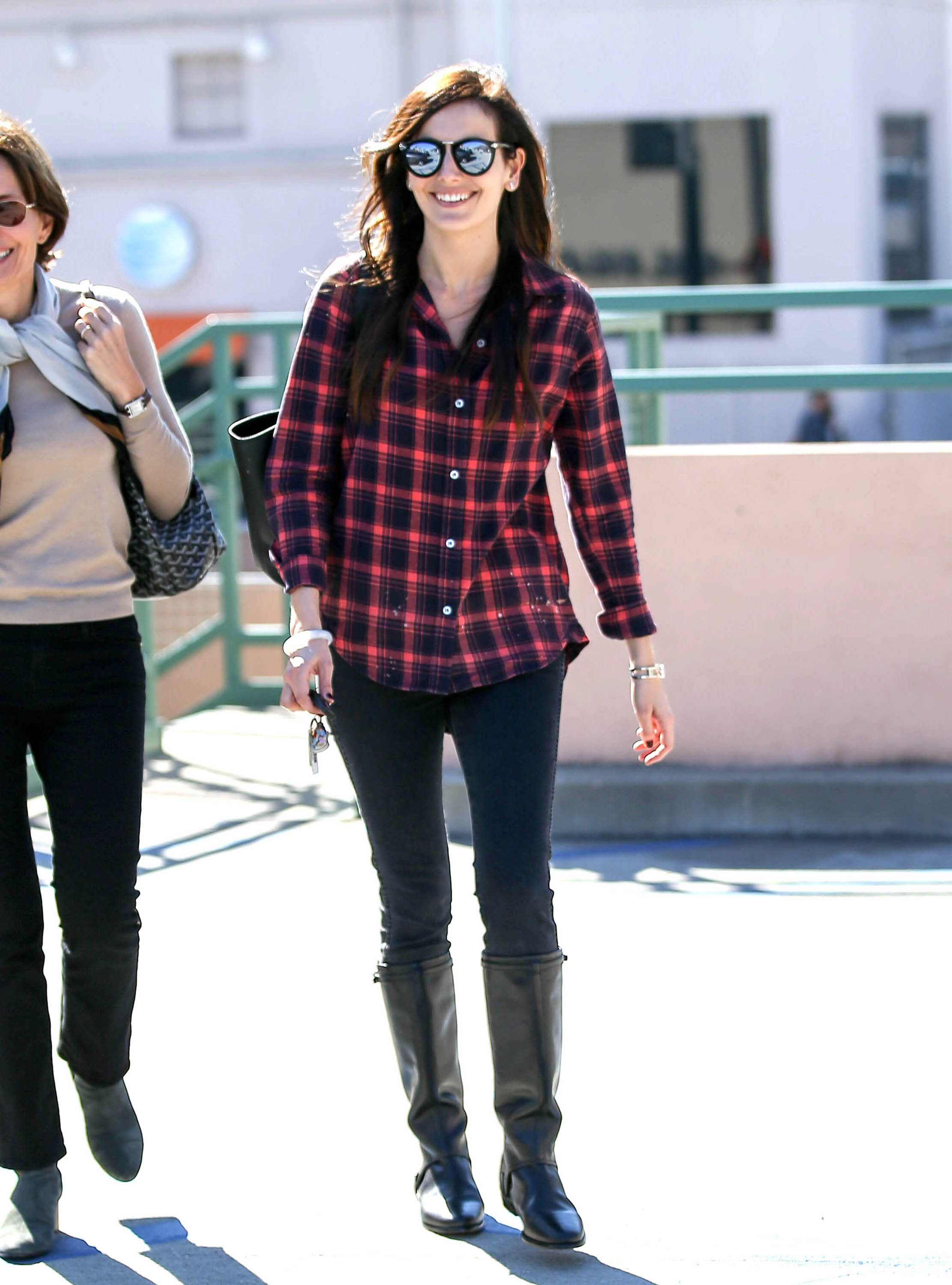 Camilla Belle looks casual and chic in a plaid shirt with black leggings and black riding boots.
