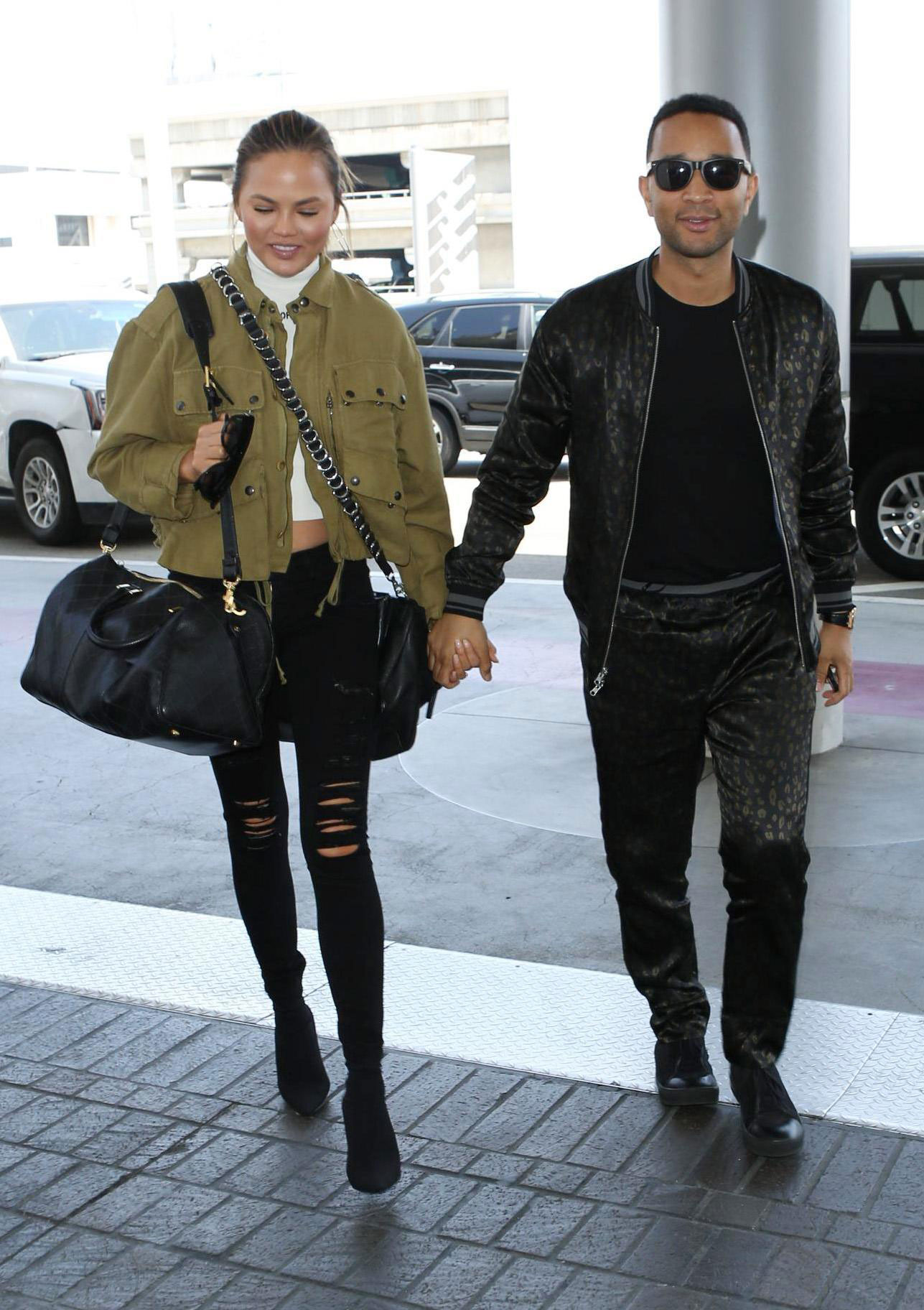 Chrissy Teigen wears a utility jacket with black ripped skinny jeans and ankle boots.