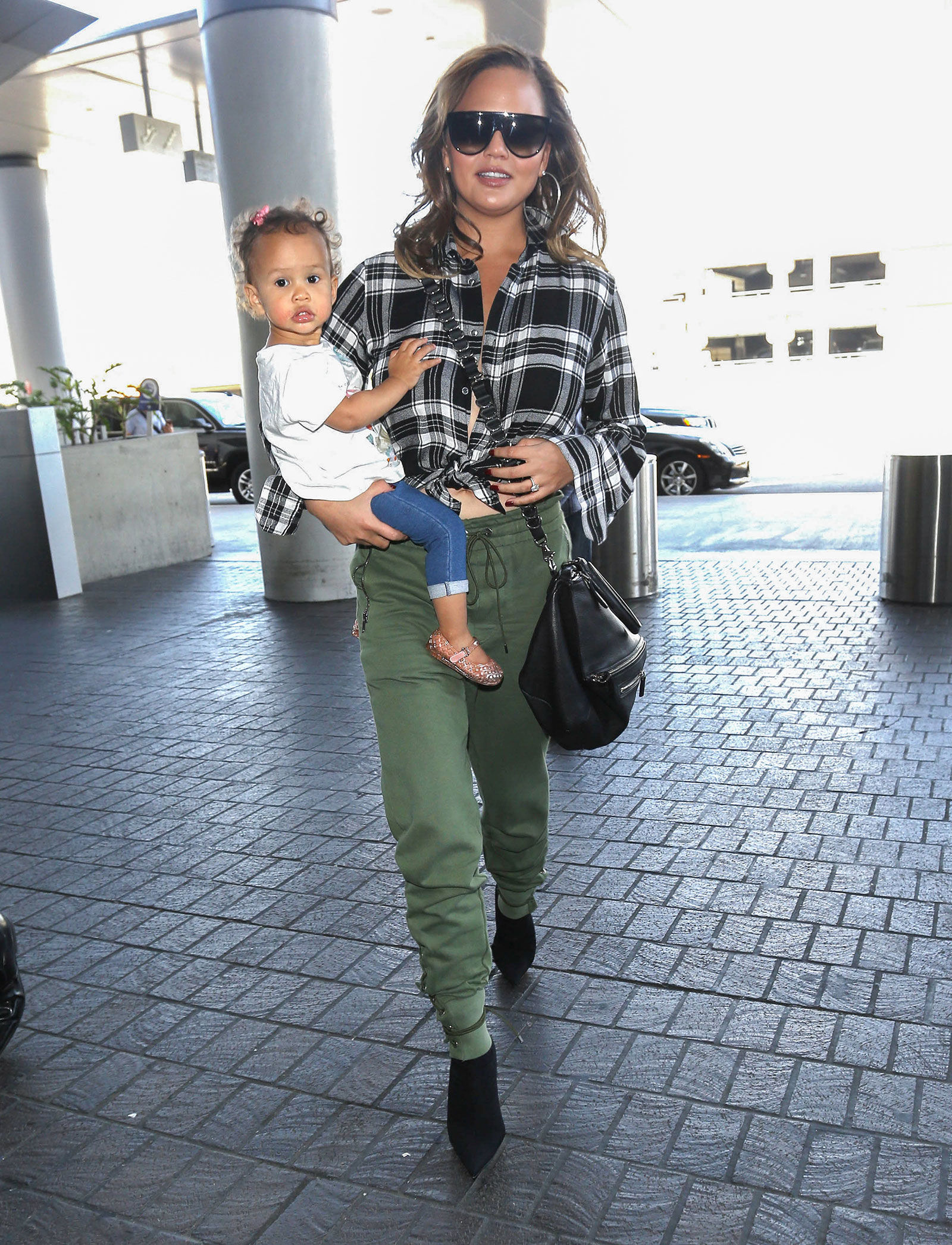 Chrissy Teigen wears a plaid shirt, olive cargo joggers and black stiletto ankle boots.