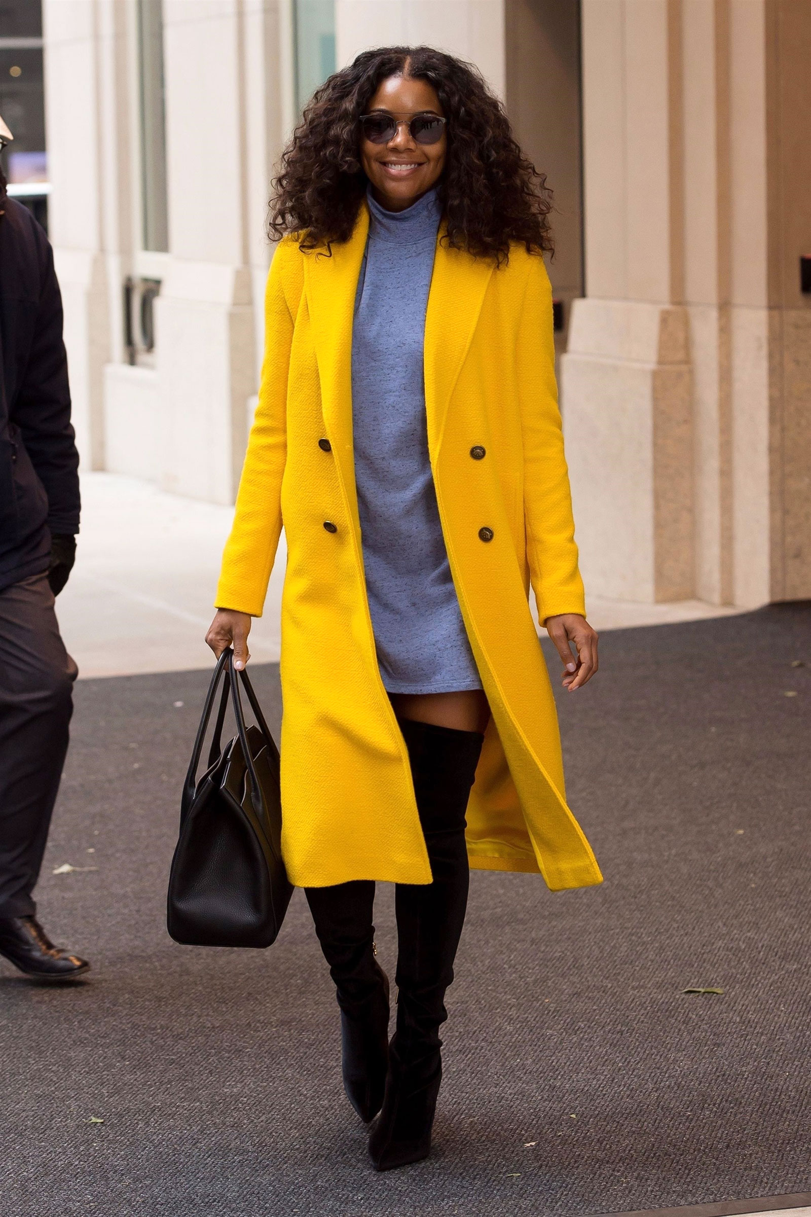 Gabrielle Union wears a bright yellow wool coat with a gray sweatedress and black over-the-knee boots.