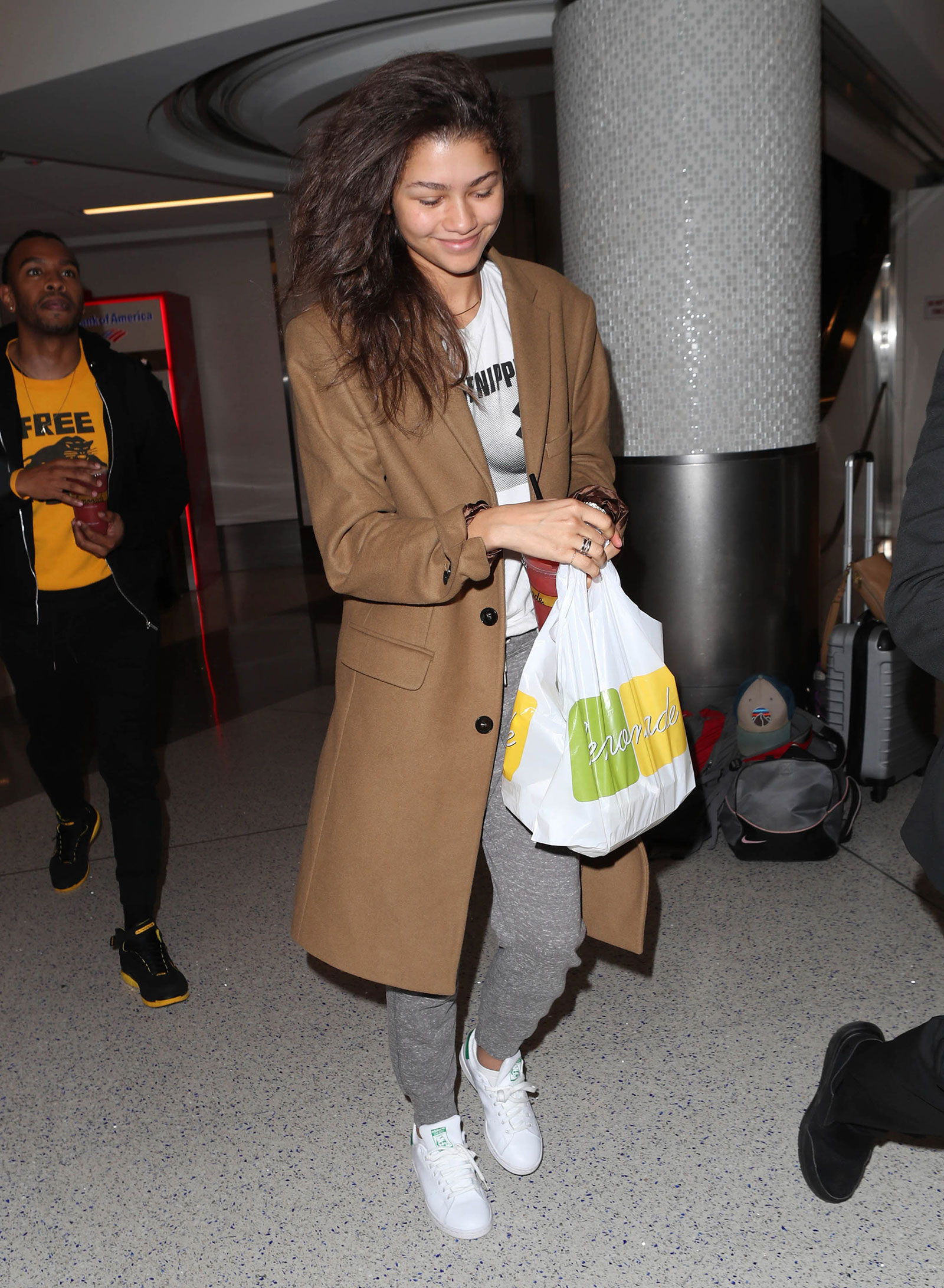Zendaya wears a camel coat with a Free the Nipple t-shirt, gray joggers and Stan Smith sneakers.