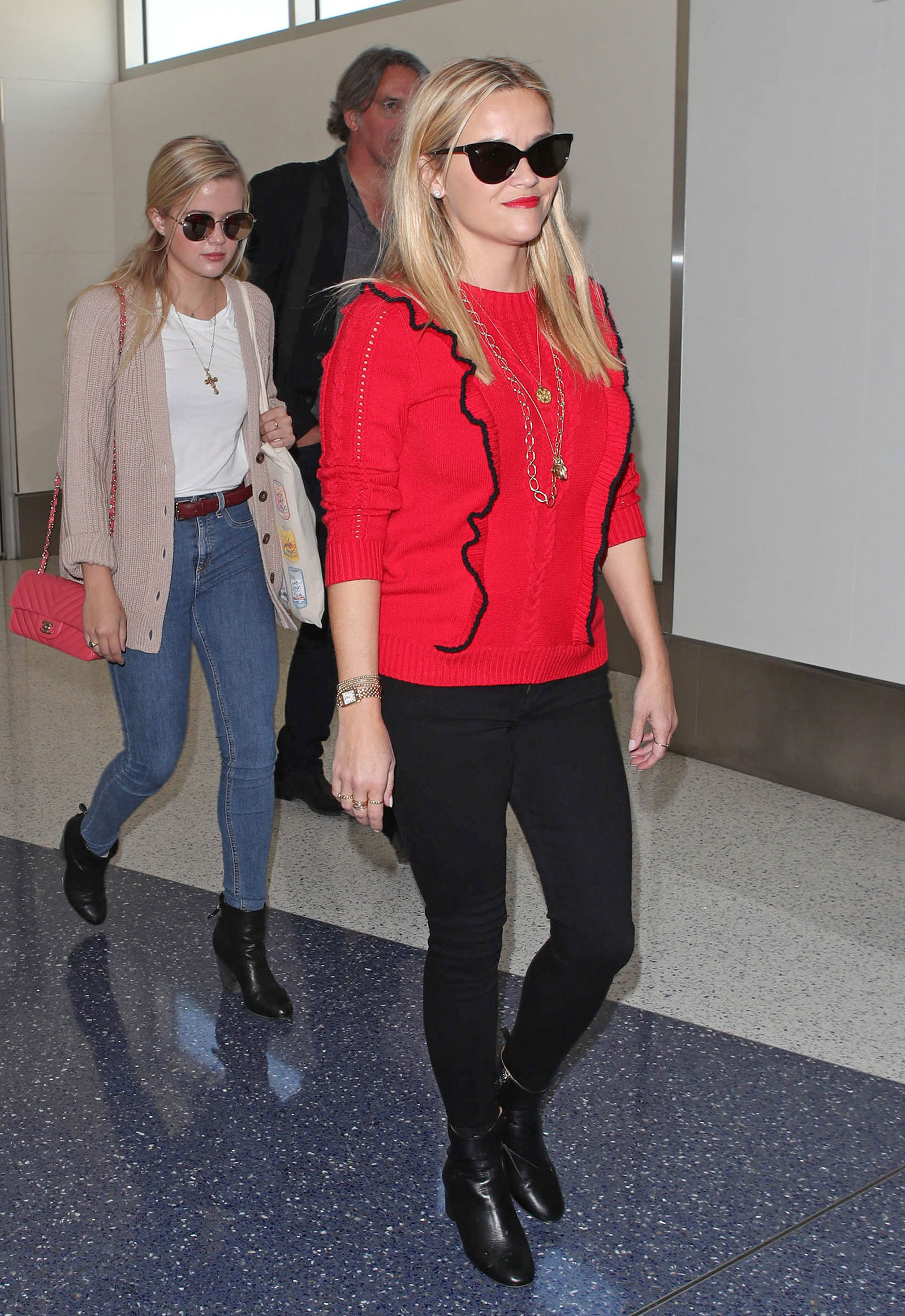 Reese Witherspoon wears a red ruffle sweater by Draper James and carries a Louis Vuitton bag while traveling through LAX.