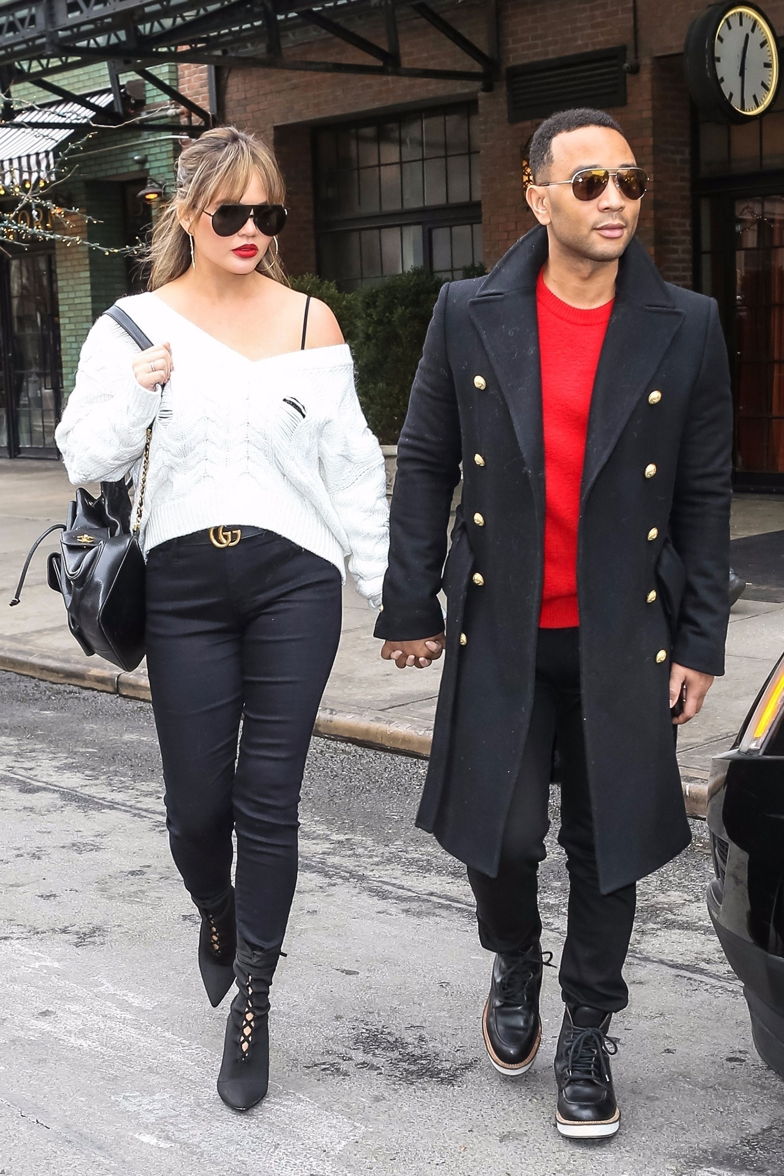 Chrissy Teigen wears a distressed white v-neck sweater with black skinny jeans and black lace-up ankle boots.