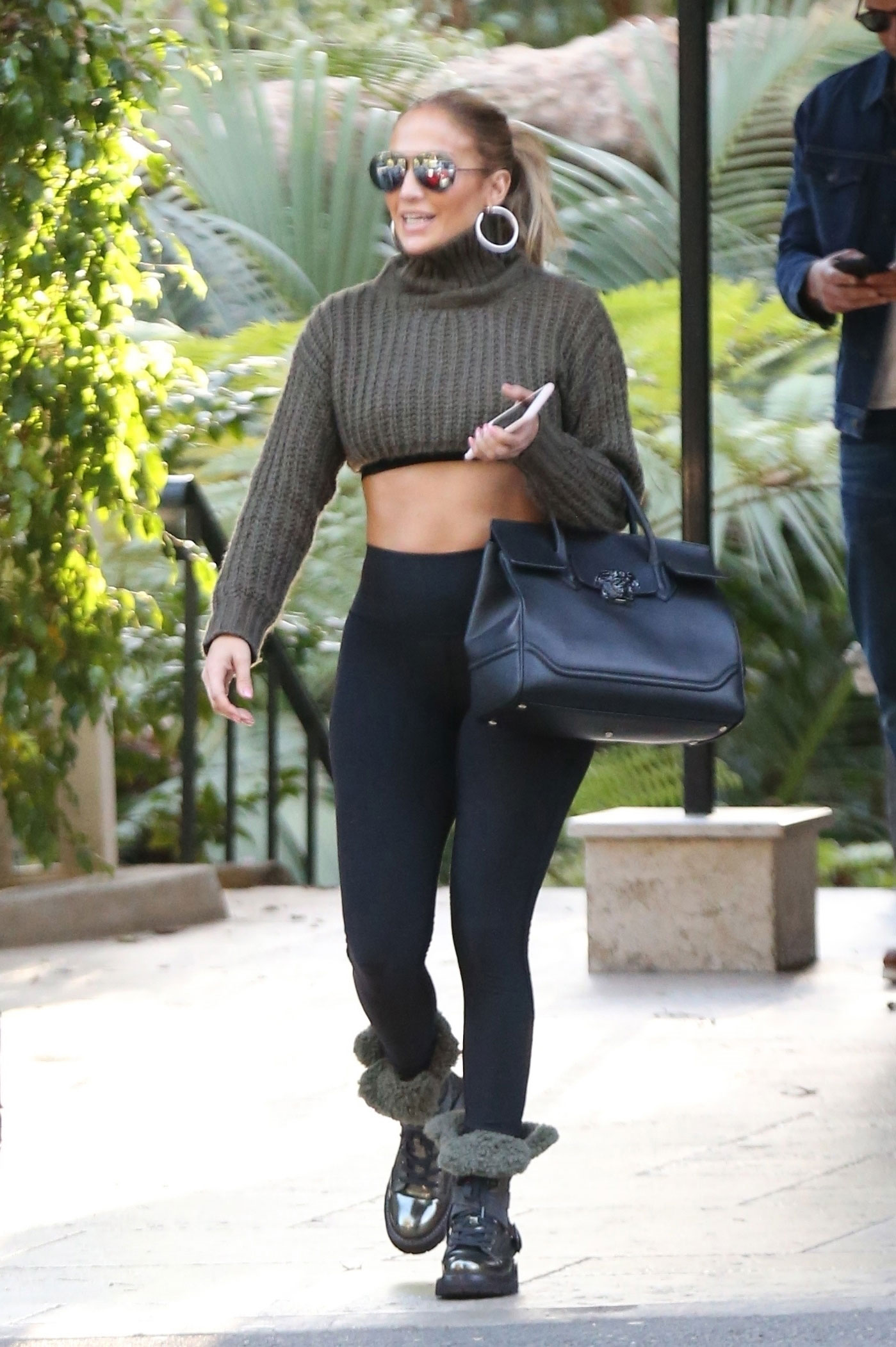 Jennifer Lopez wears a crop turtleneck sweater with Alo Yoga leggings and a Versace bag.