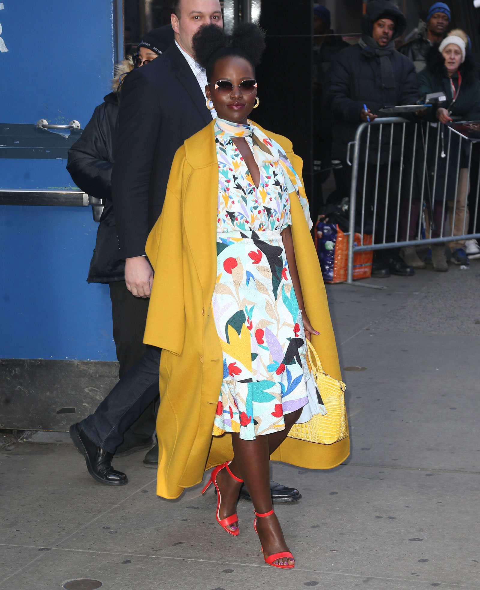 Lupita Nyong'o in floral dress, yellow coat and red strappy heels by Nine West
