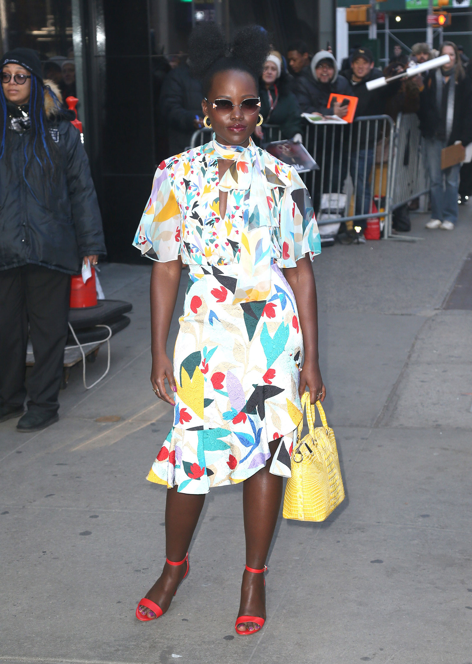 Lupita Nyong'o in floral dress, yellow coat and red strappy heels by Nine West