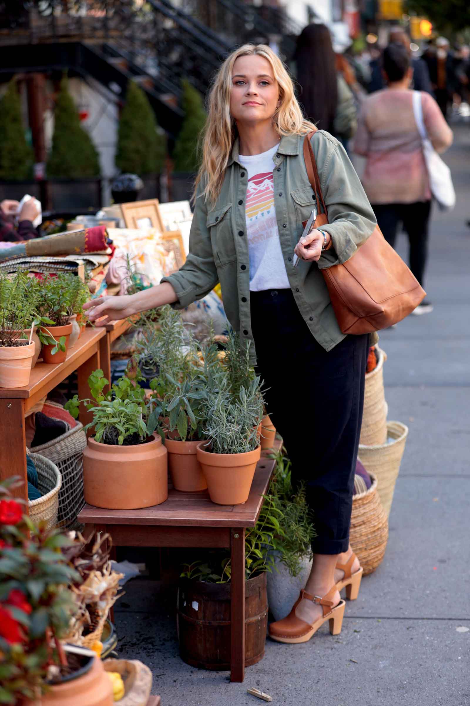Reese Witherspoon looks cute and casual in an army green utility jacket, black pants, graphic tee and cognac accessories.